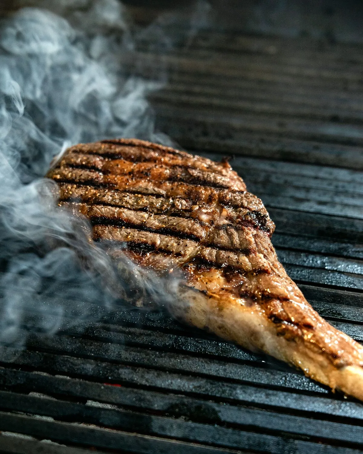 A thick ribeye cooking on a smoky grill
